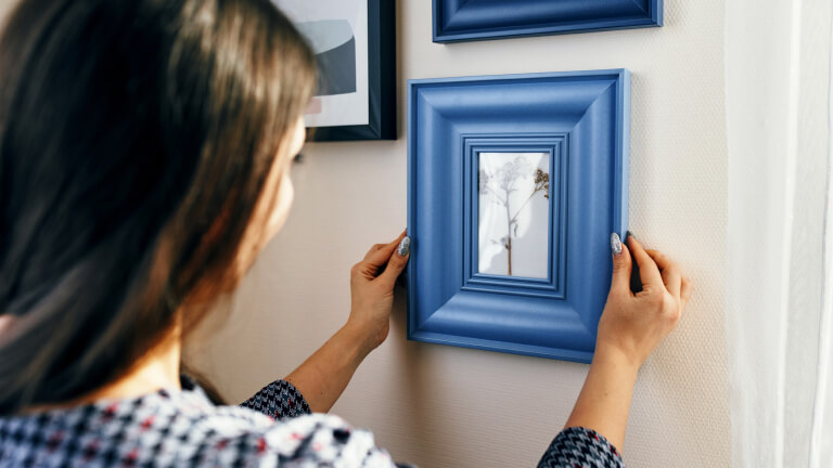 Close-up young woman apartment, hangs frames on the walls.